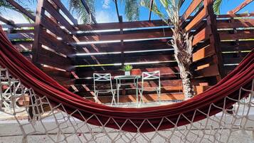 A hammock with a view of a wooden structure, a small table, and chairs.
