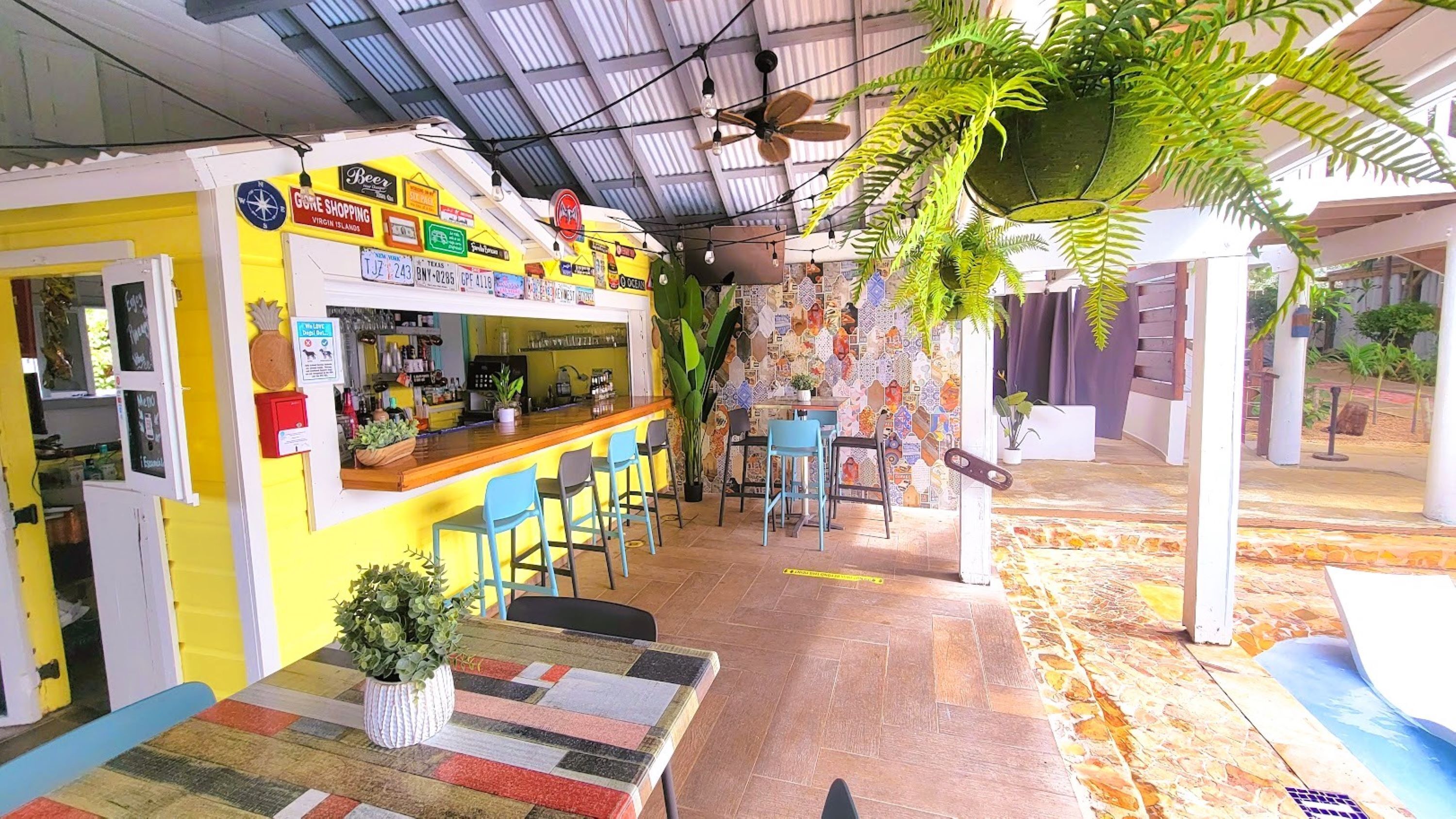 A bar area with a yellow and white color scheme, a counter, bar stools, and hanging plants.