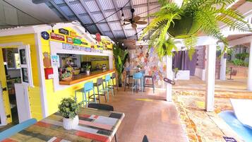 A bar area with a yellow and white color scheme, a counter, bar stools, and hanging plants.