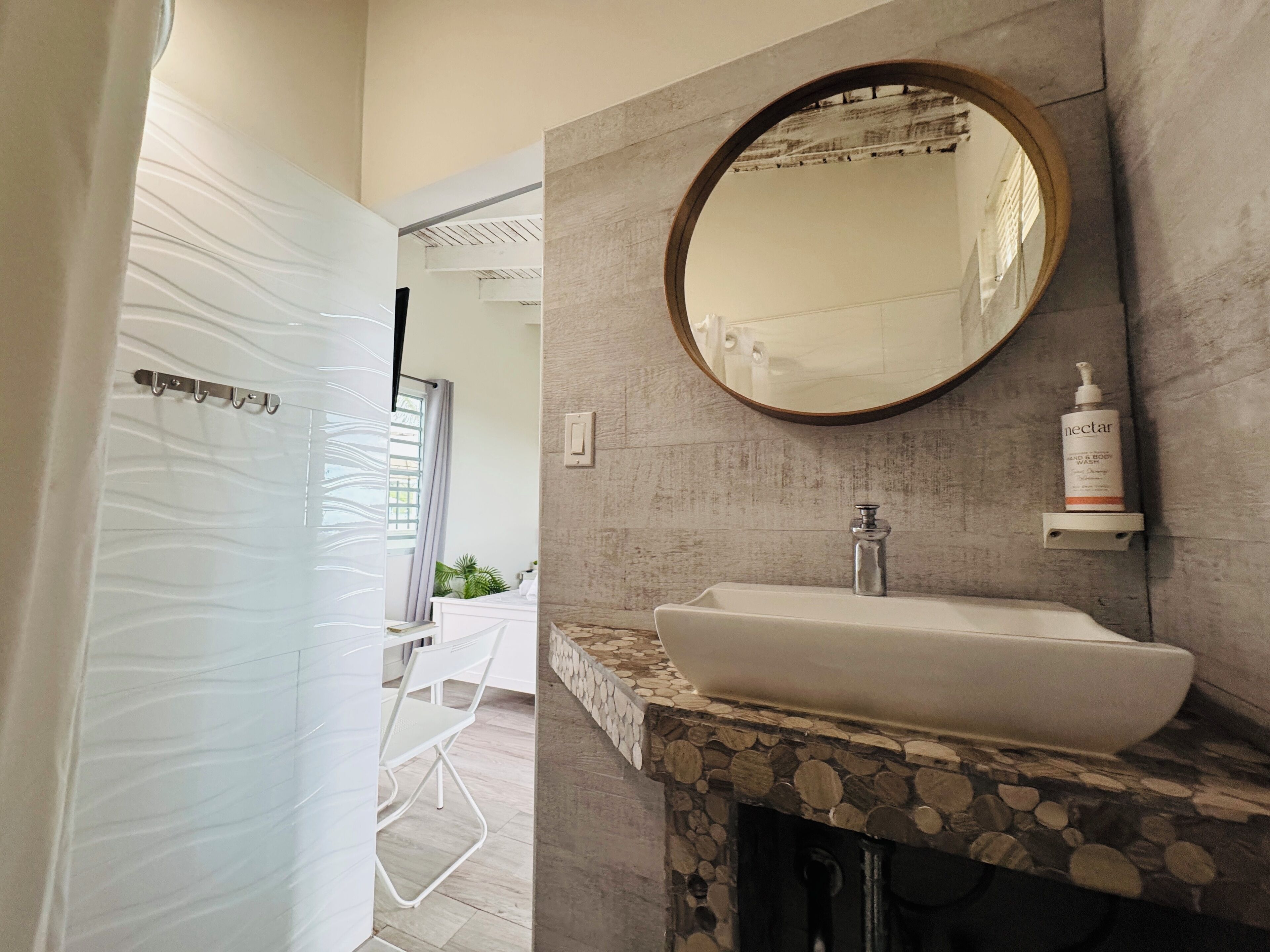 A bathroom with a stone sink, a round mirror, and a bottle of Nectar body wash.