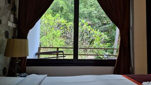 A hotel room with a bed, a window with curtains, and a view of greenery outside. - Chaweng Park Place (Koh Samui)