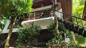 A two-story building with a balcony, surrounded by lush greenery and a stone wall. - Chaweng Park Place (Koh Samui)