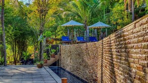 A brick wall with a water feature, outdoor seating with umbrellas, and lush greenery. - Chaweng Park Place (Koh Samui)