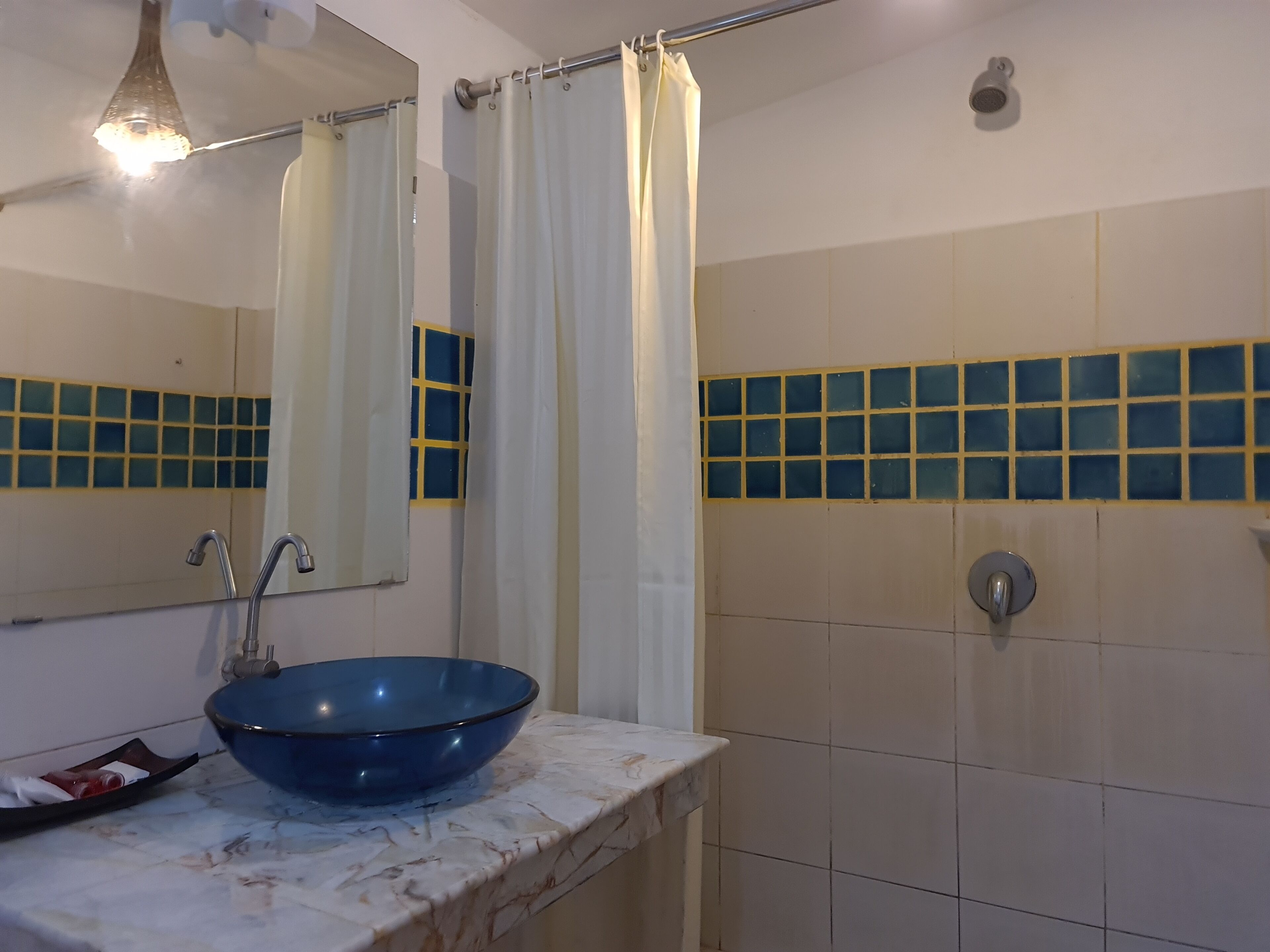 A bathroom with a blue basin, a mirror, a shower curtain, and tiled walls.