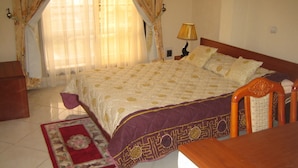 Een netjes ingerichte slaapkamer met een groot bed, een houten nachtkastje, een lamp en een rood bloemenkleed.