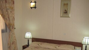 Een slaapkamer met een bed, twee bedlampjes, een nachtkastje, een lijst met een afbeelding aan de muur en een gordijn.