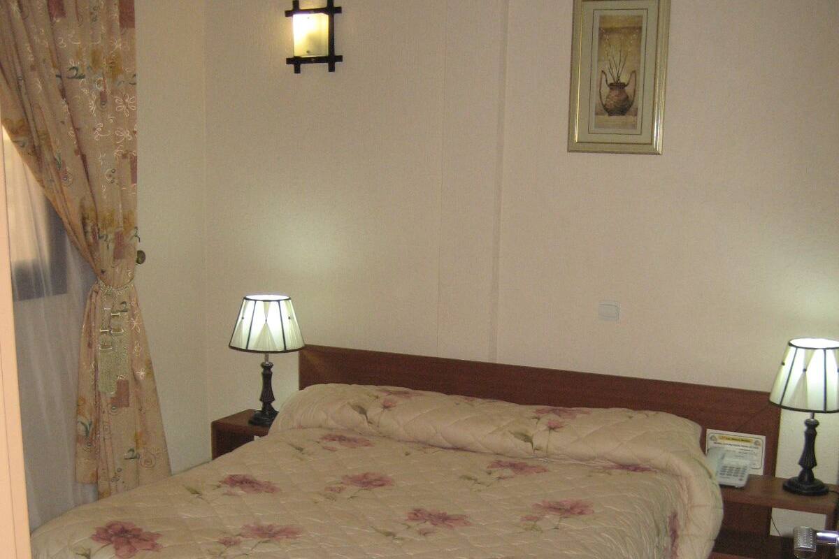 A bedroom with a bed, two bedside lamps, a nightstand, a framed picture on the wall, and a curtain.