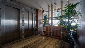 Un ascensor moderno con puertas metálicas, suelo de madera y un arreglo decorativo de plantas.