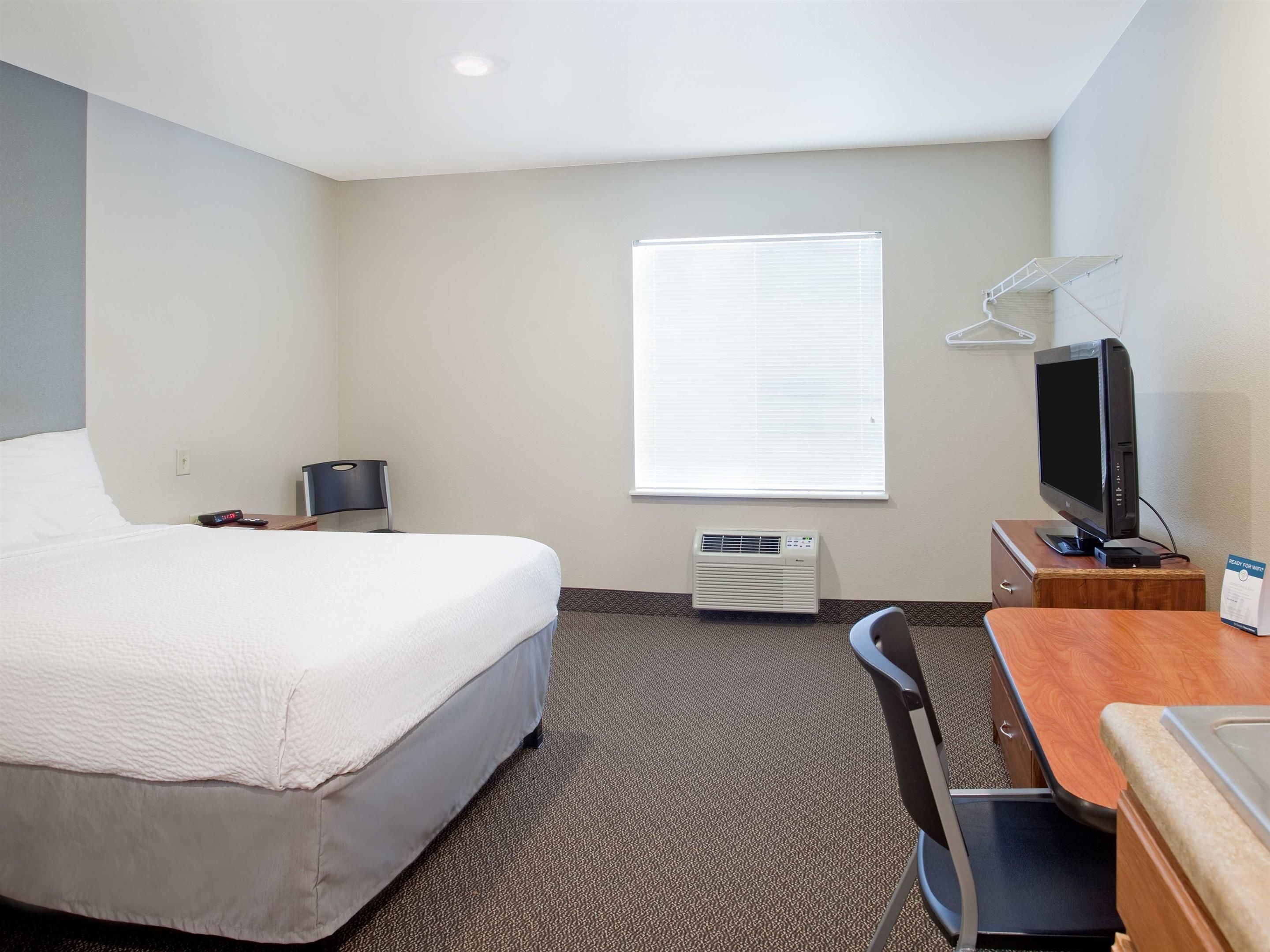 A hotel room with a bed, a desk, a chair, a television, and an air conditioning unit.