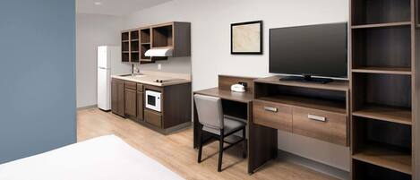 A compact hotel room with a kitchenette, a bed, a desk, and a TV.