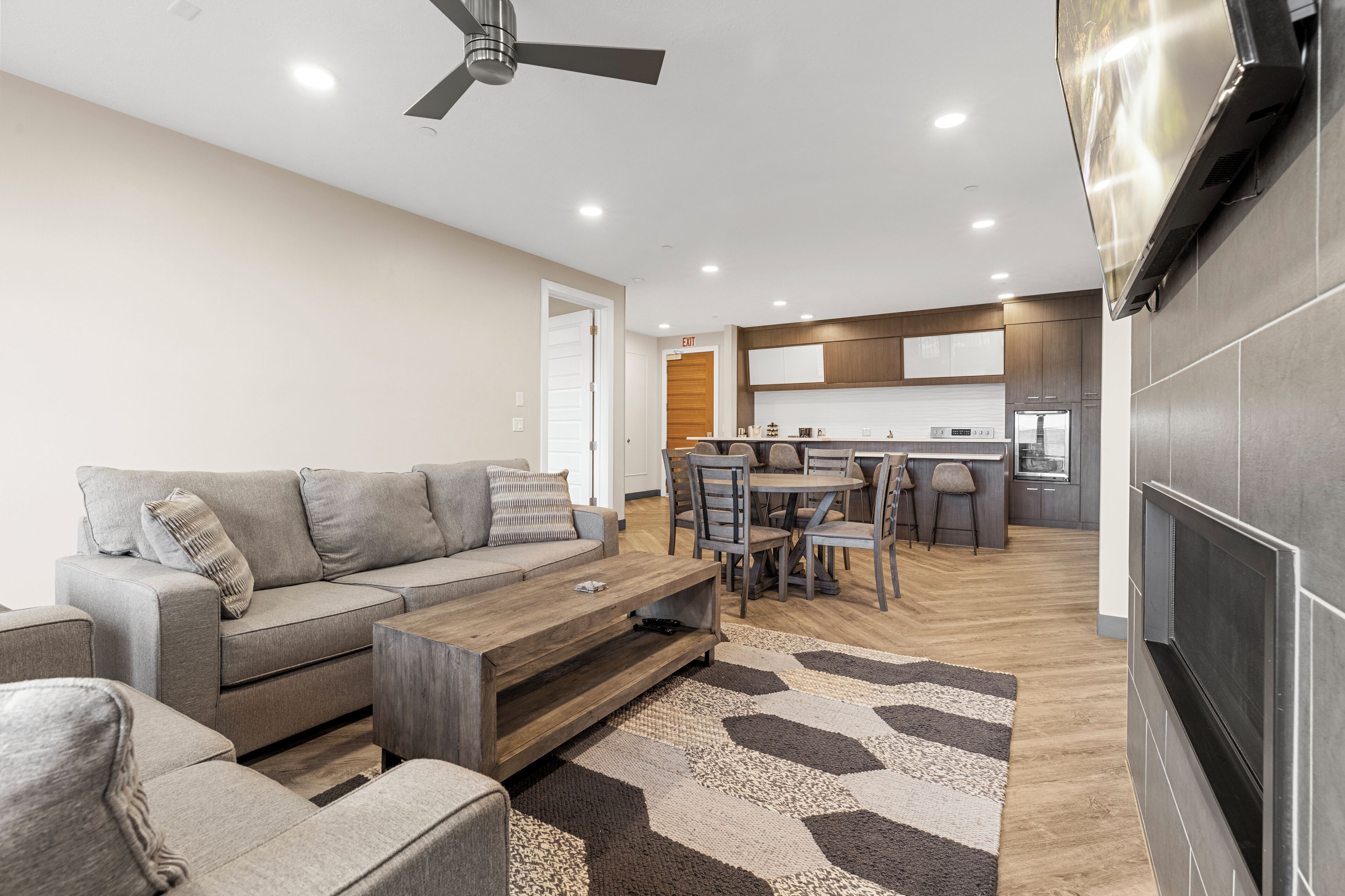 A modern living room with a sofa, coffee table, and TV, leading to a kitchen area with a dining set.