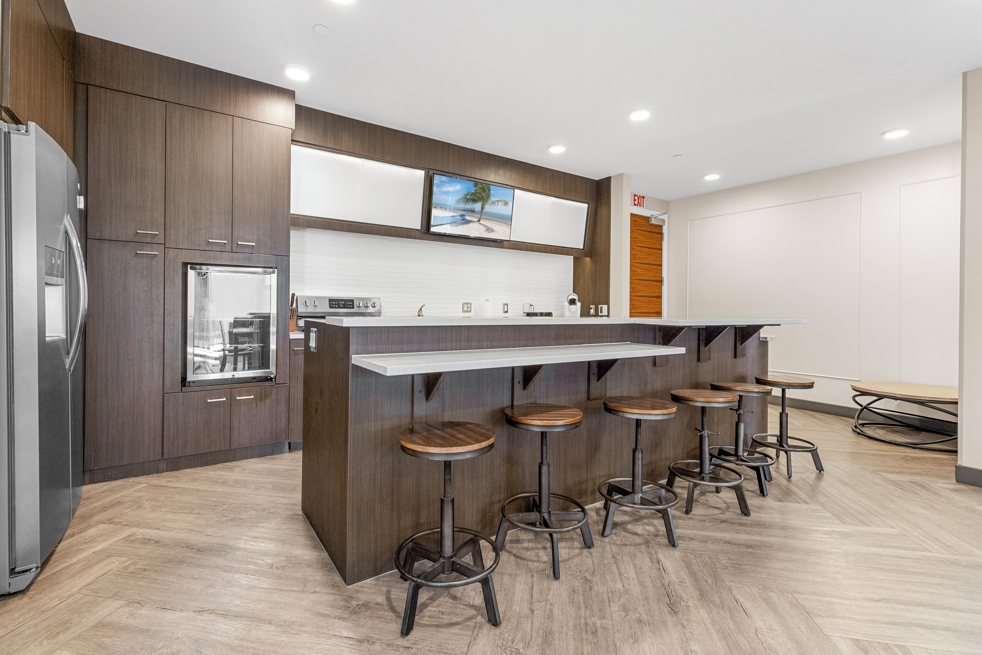 A modern kitchen with a central island, bar stools, and a refrigerator.