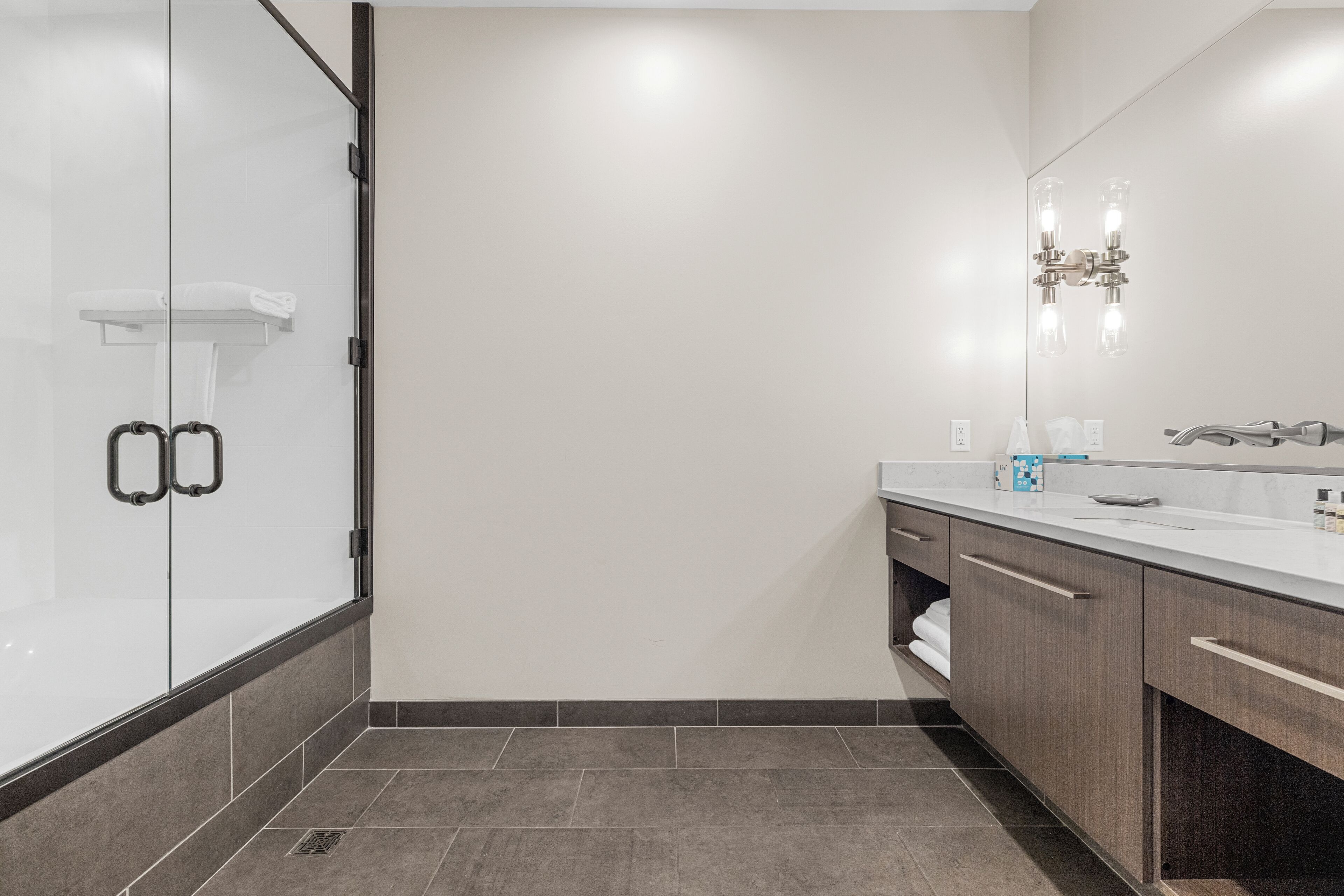 Een moderne badkamer met een glazen douchecabine, een grote spiegel en een wastafel met aanrechtblad.