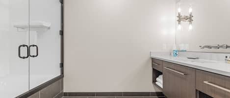 Un baño moderno con cabina de ducha de vidrio, un espejo grande y un tocador con encimera.