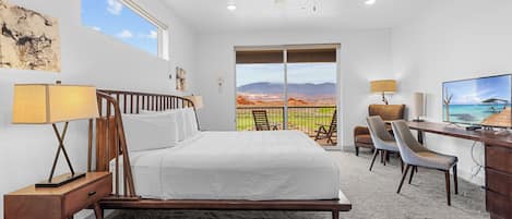 A bedroom with a bed, desk, and chairs, a ceiling fan, and a large window with a mountain view.