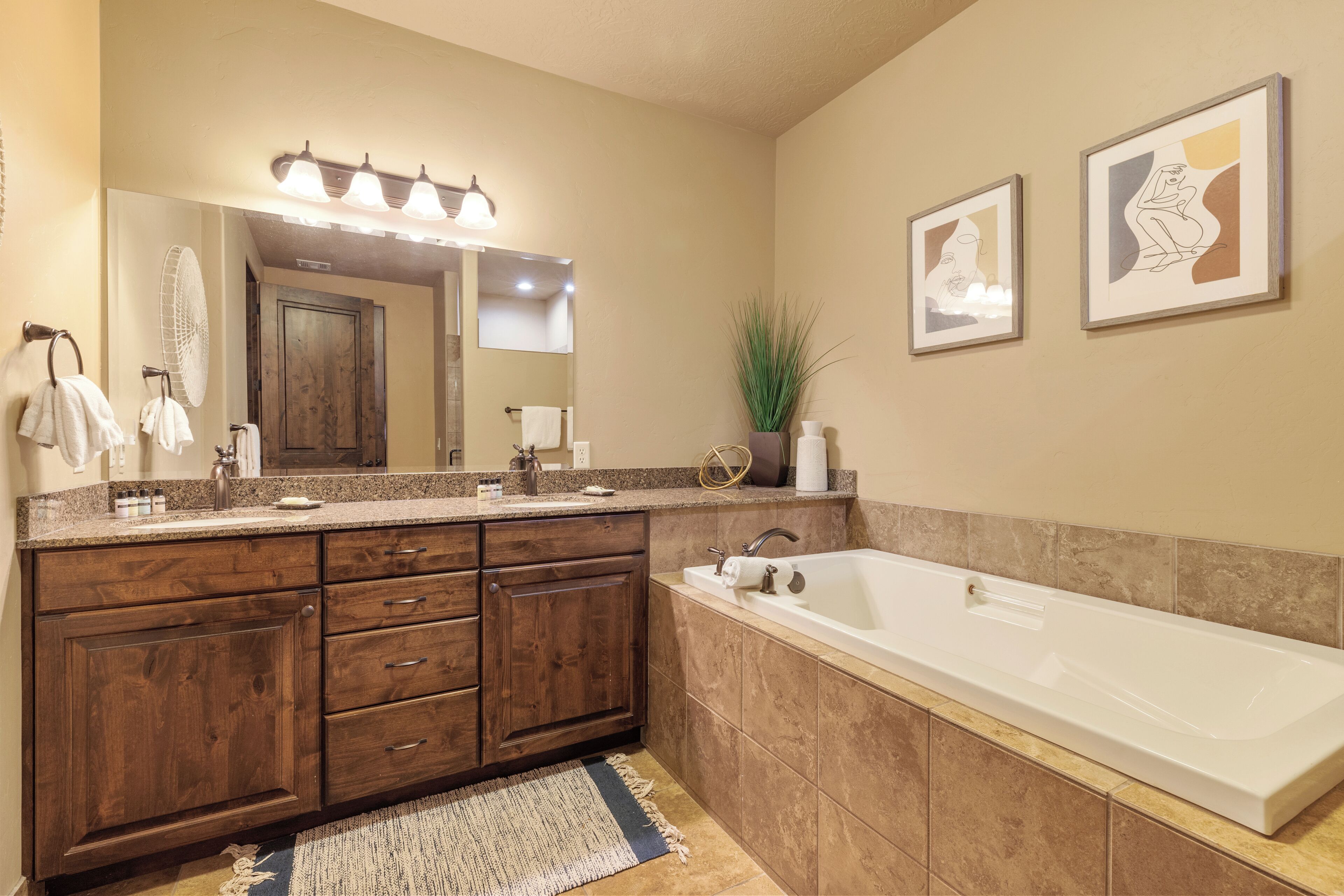 A modern bathroom with a large vanity, a bathtub, and two framed artworks on the wall.