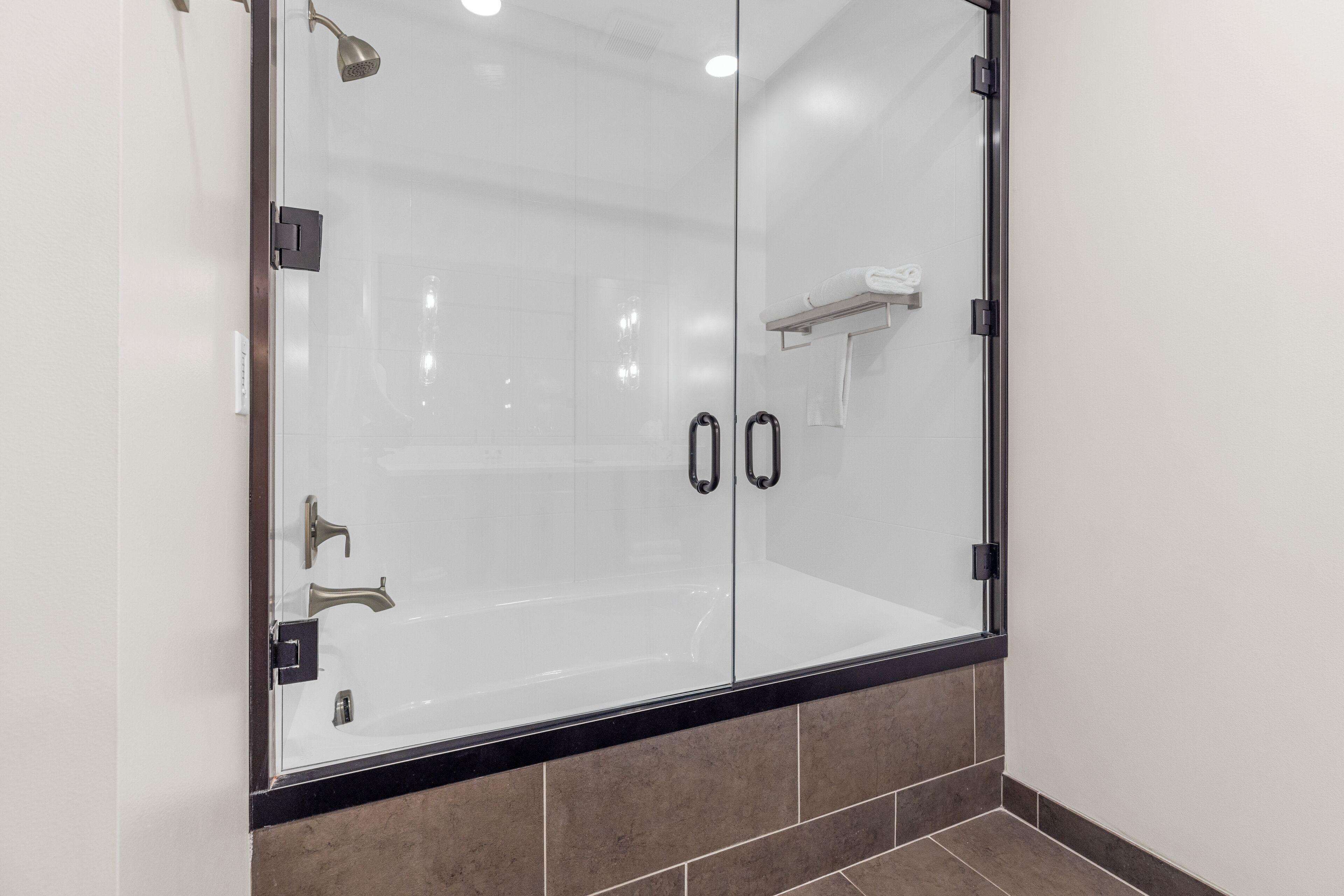 Un espace douche clos par des parois de verre, avec un cadre noir, un porte-serviettes et un distributeur de serviettes fixé au mur.