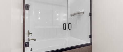 A glass-enclosed shower area with a black frame, a towel rack, and a wall-mounted towel dispenser.