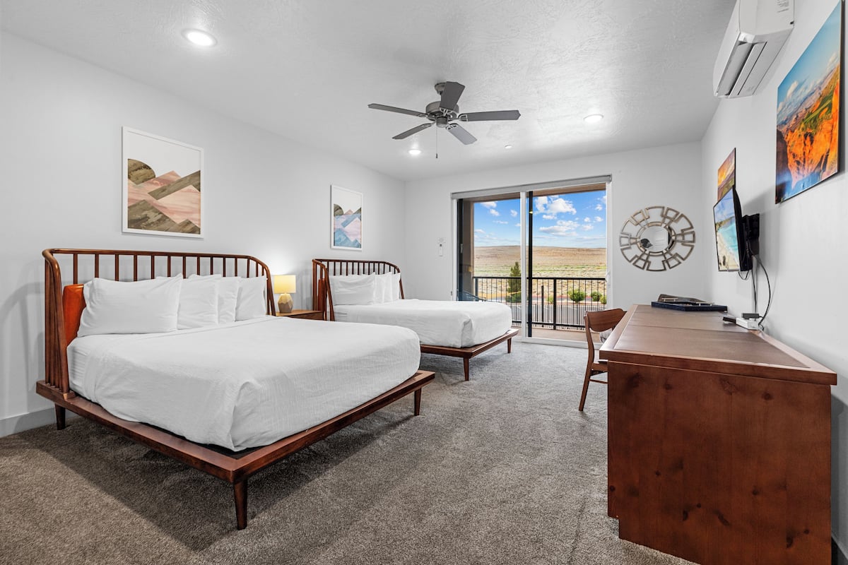 A bedroom with two beds, a desk, and a balcony with a view.