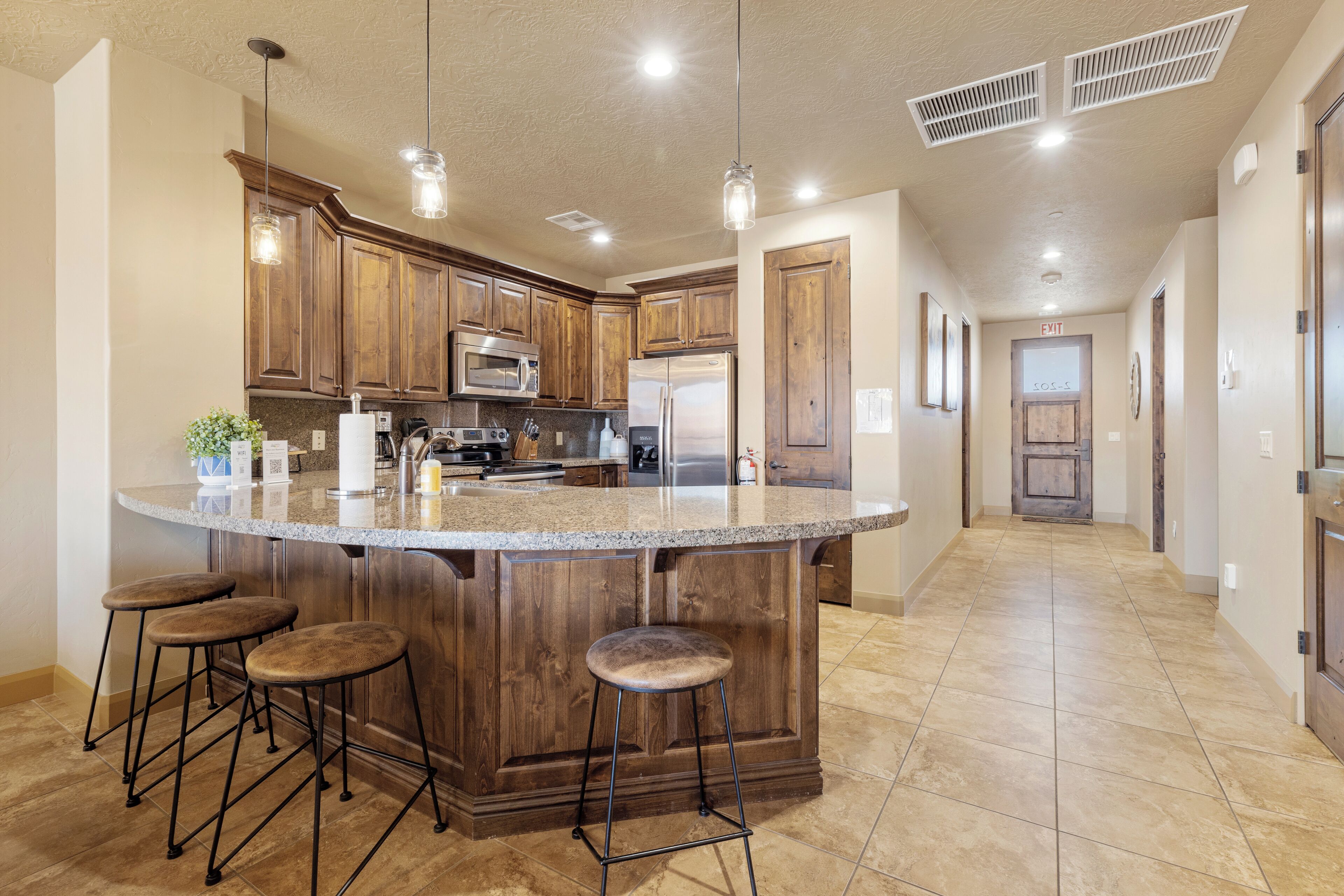 A spacious kitchen with a large island, wooden cabinets, stainless steel appliances, and pendant lighting.