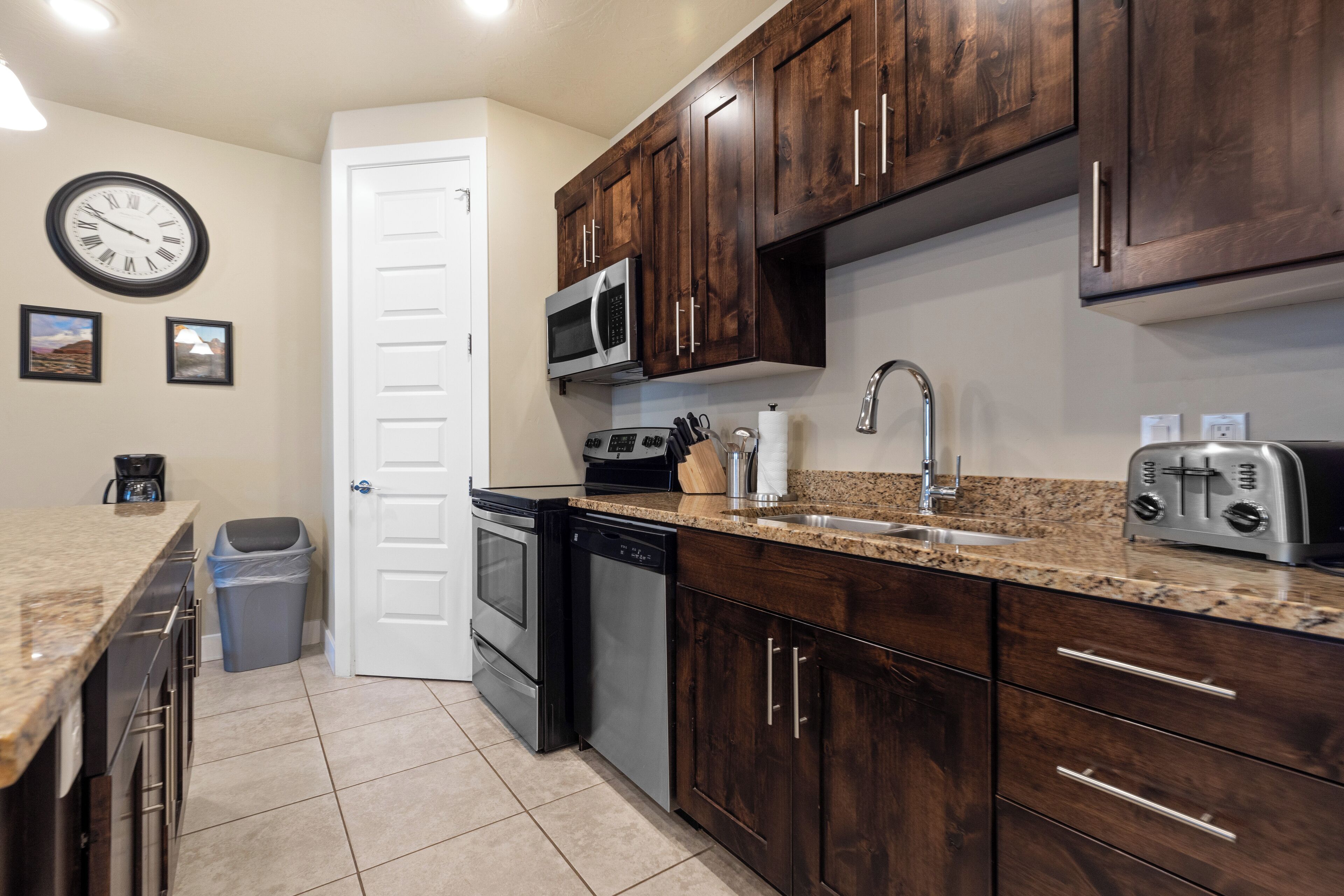 A kitchen with dark wooden cabinets, a stainless steel microwave, a dishwasher, and a granite countertop.