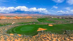 A golf course with multiple greens and sand bunkers, surrounded by desert vegetation and mountains in the background. - Vacation Rentals at Sand Hollow Resort (Hurricane)