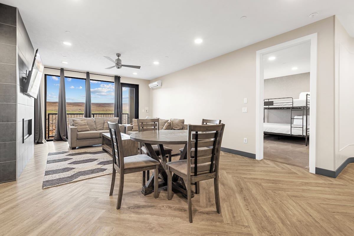 A modern living room with a dining area, large windows, and a view of the landscape.