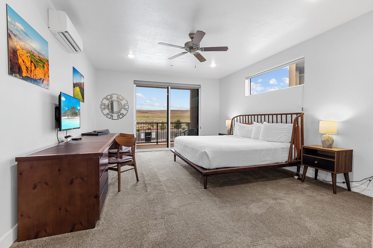 A bedroom with a bed, desk, chair, and a large window.