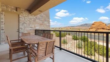 A balcony with a stone wall, a wooden table and chairs, and a view of a desert landscape.