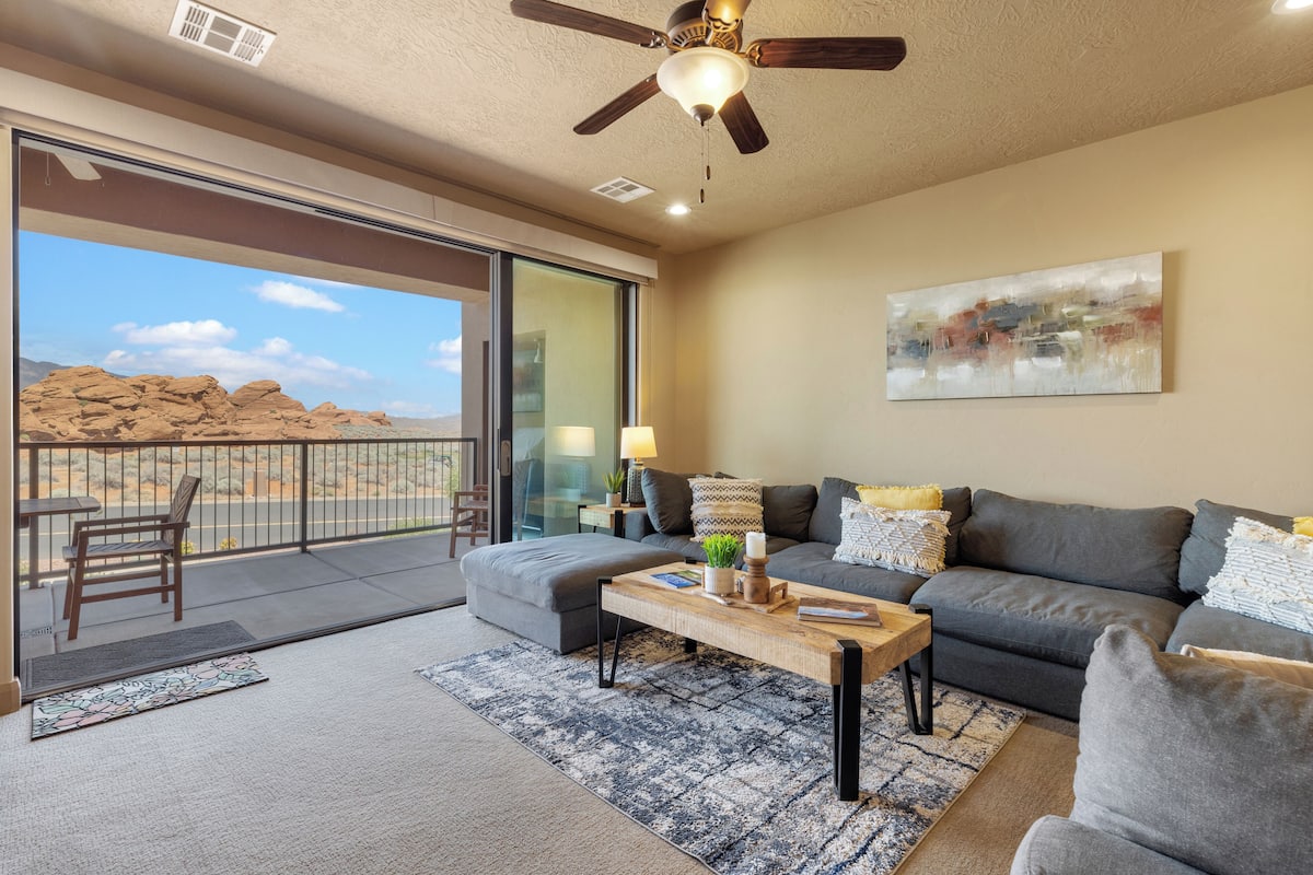 A living room with a sofa, coffee table, and a balcony with a view of the desert.