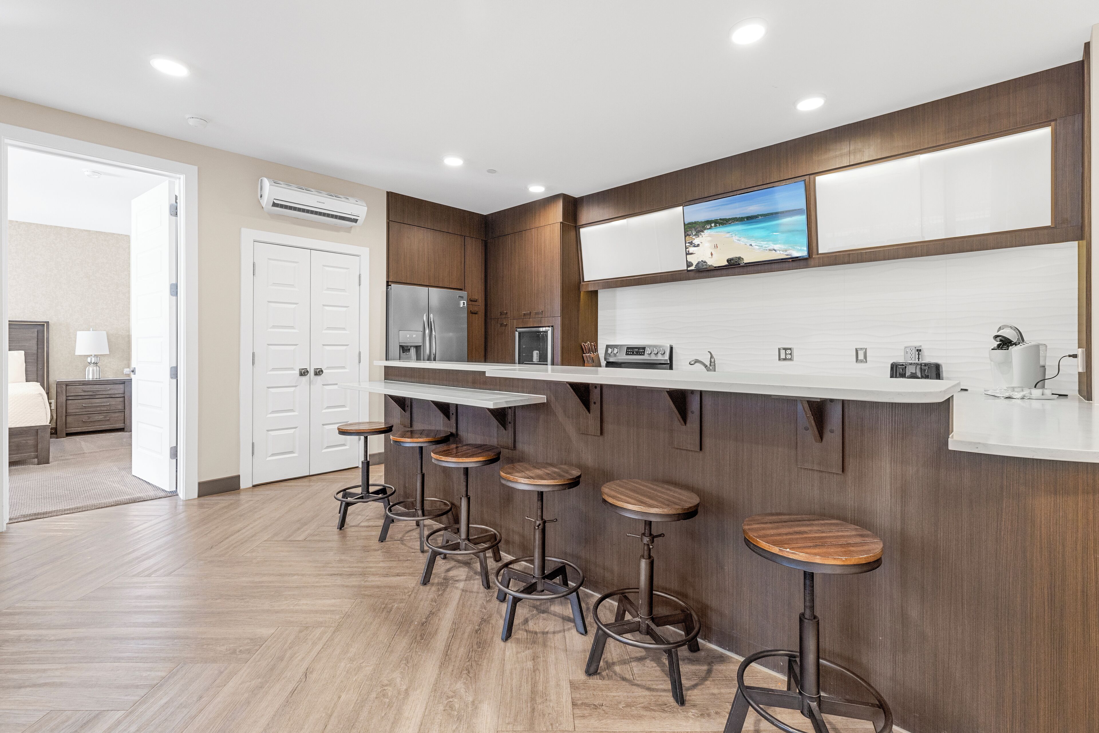 A modern kitchen with a long counter, bar stools, and a large TV mounted above the counter.