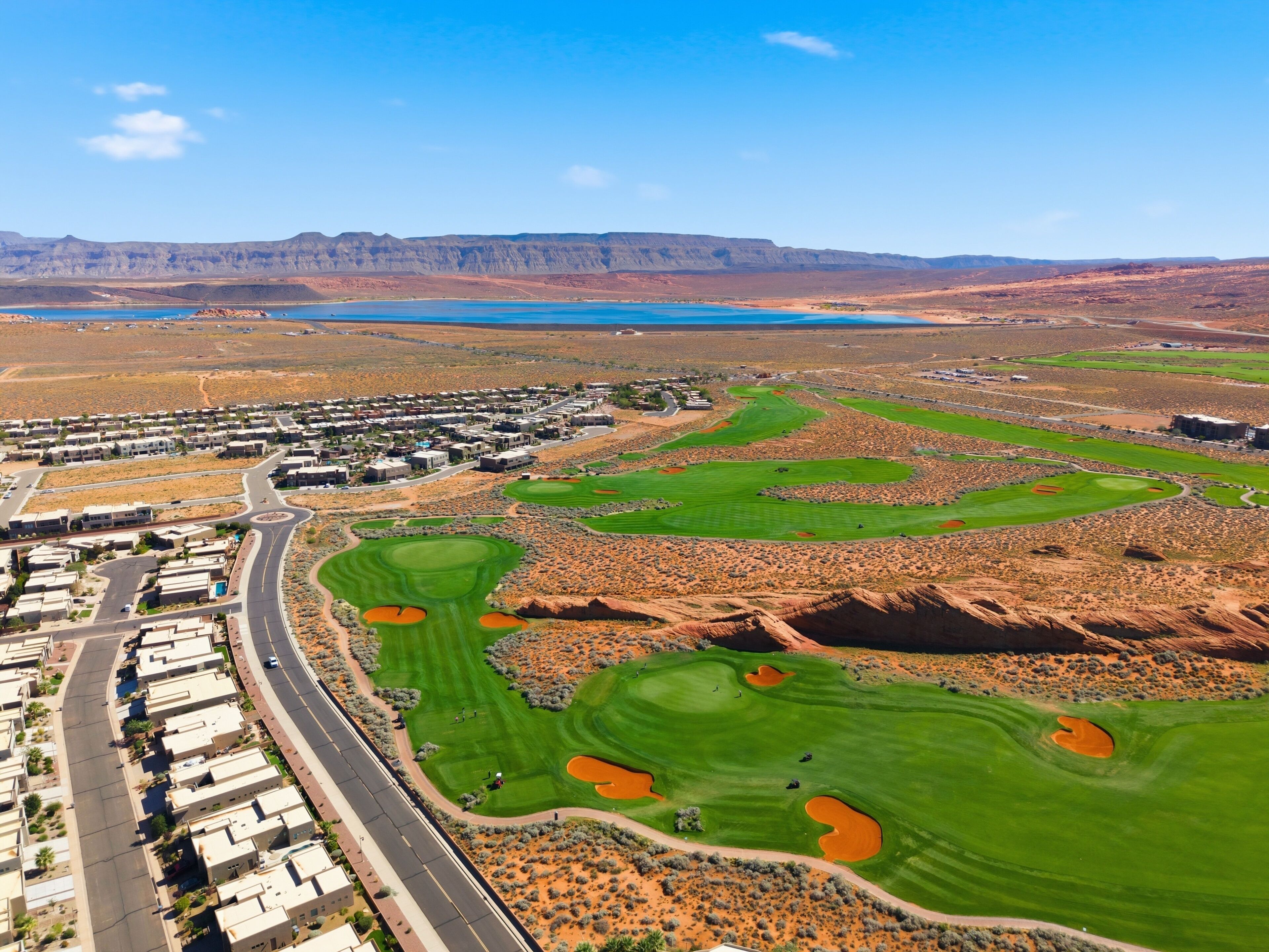 A golf course with a residential area, a road, and distant mountains.