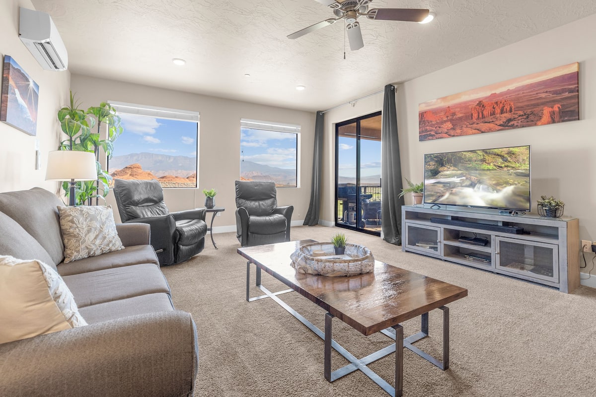 A spacious living room with a sofa, chairs, a coffee table, and a TV on a stand.