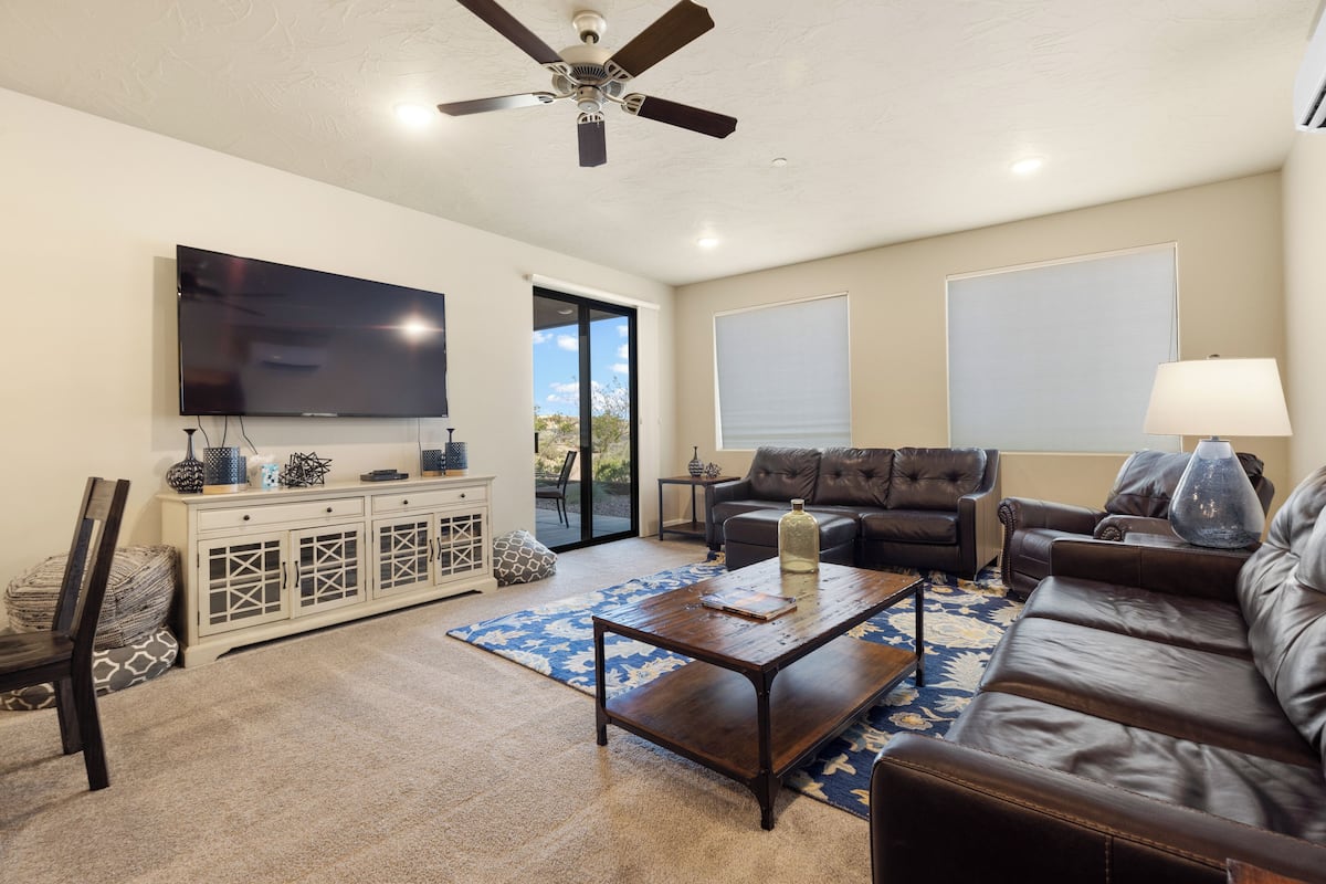 A living room with a flat-screen TV, leather sofas, a coffee table, and a ceiling fan.