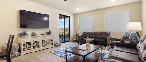 A living room with a flat-screen TV, leather sofas, a coffee table, and a ceiling fan.