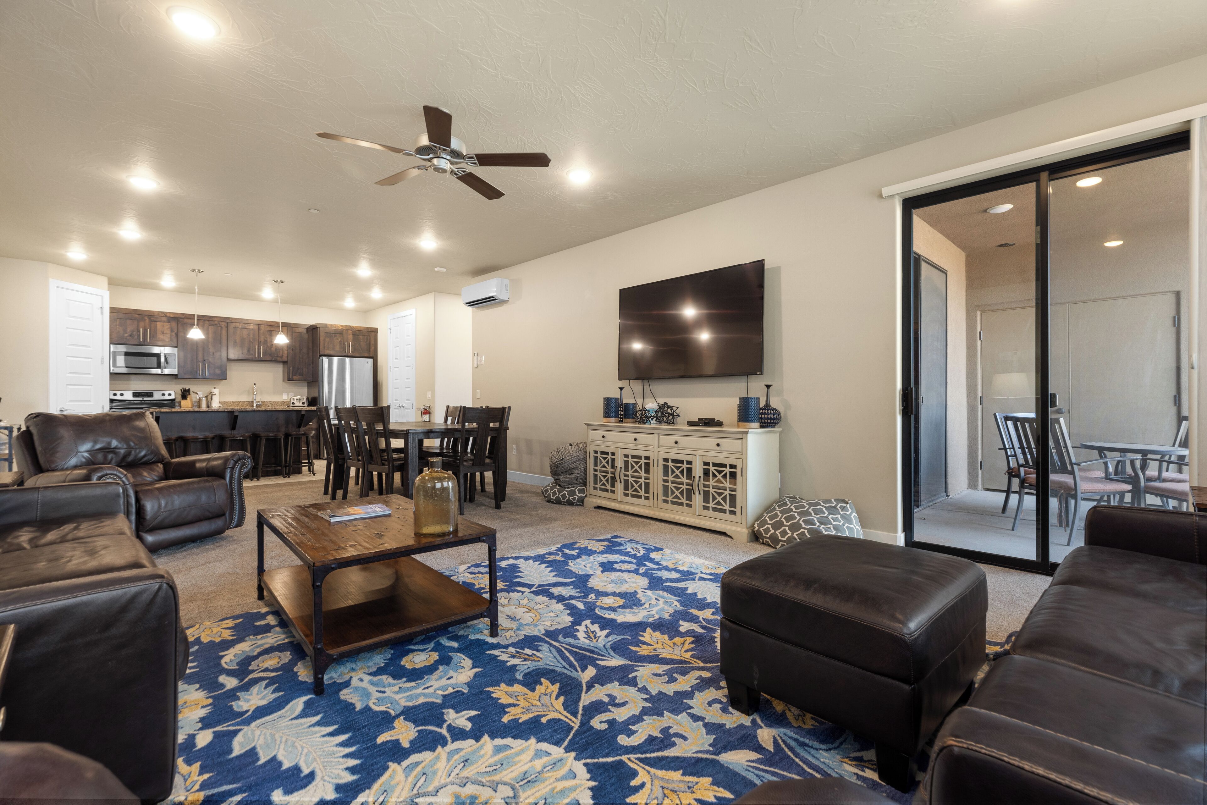 A spacious living room with a large blue patterned rug, leather sofas, a coffee table, and a ceiling fan.