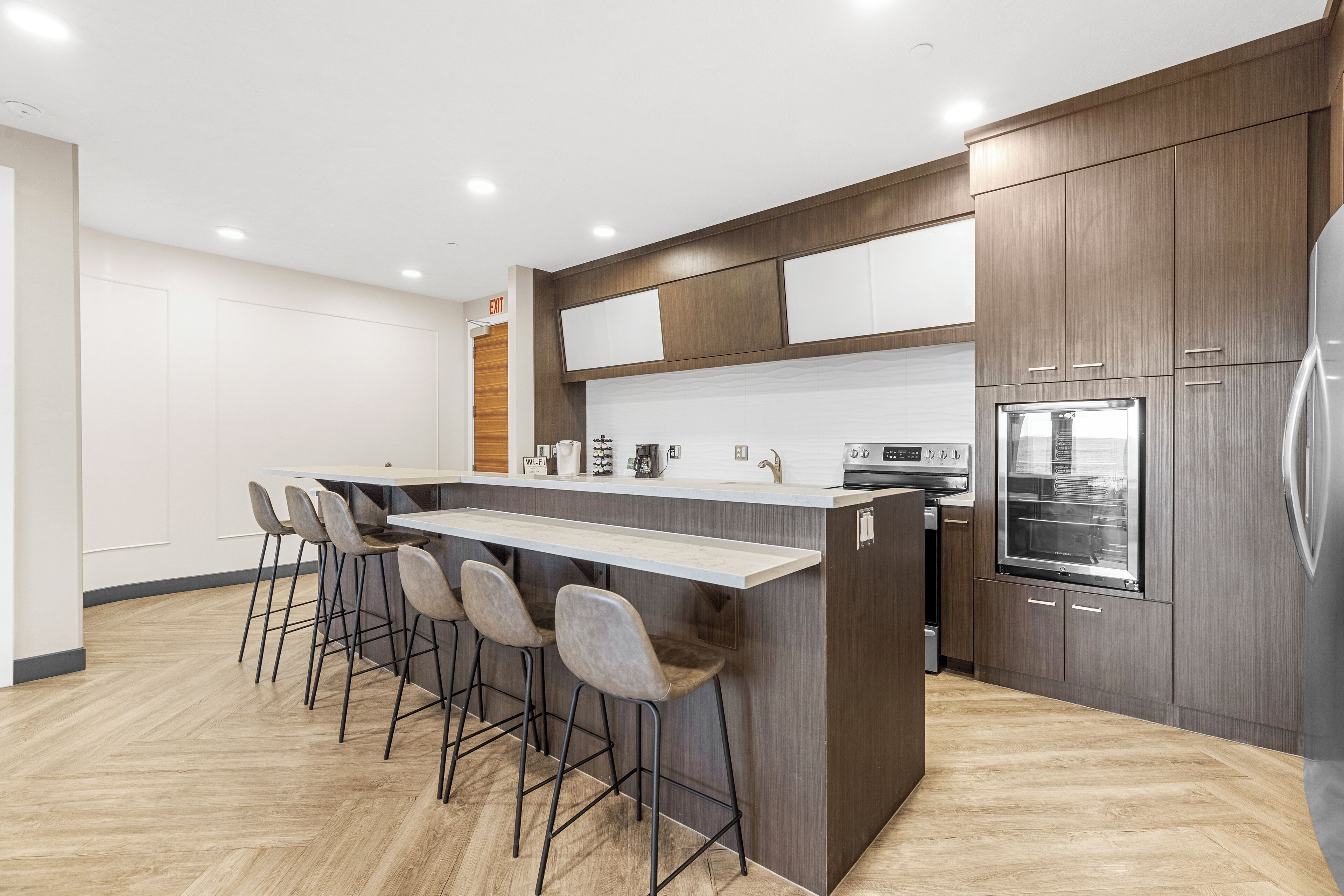 A modern kitchen with a central island, bar stools, wooden cabinets, and built-in appliances.