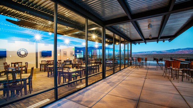 An outdoor dining area with glass walls, wooden tables, and chairs, overlooking a mountainous landscape. - Vacation Rentals at Sand Hollow Resort (Hurricane)