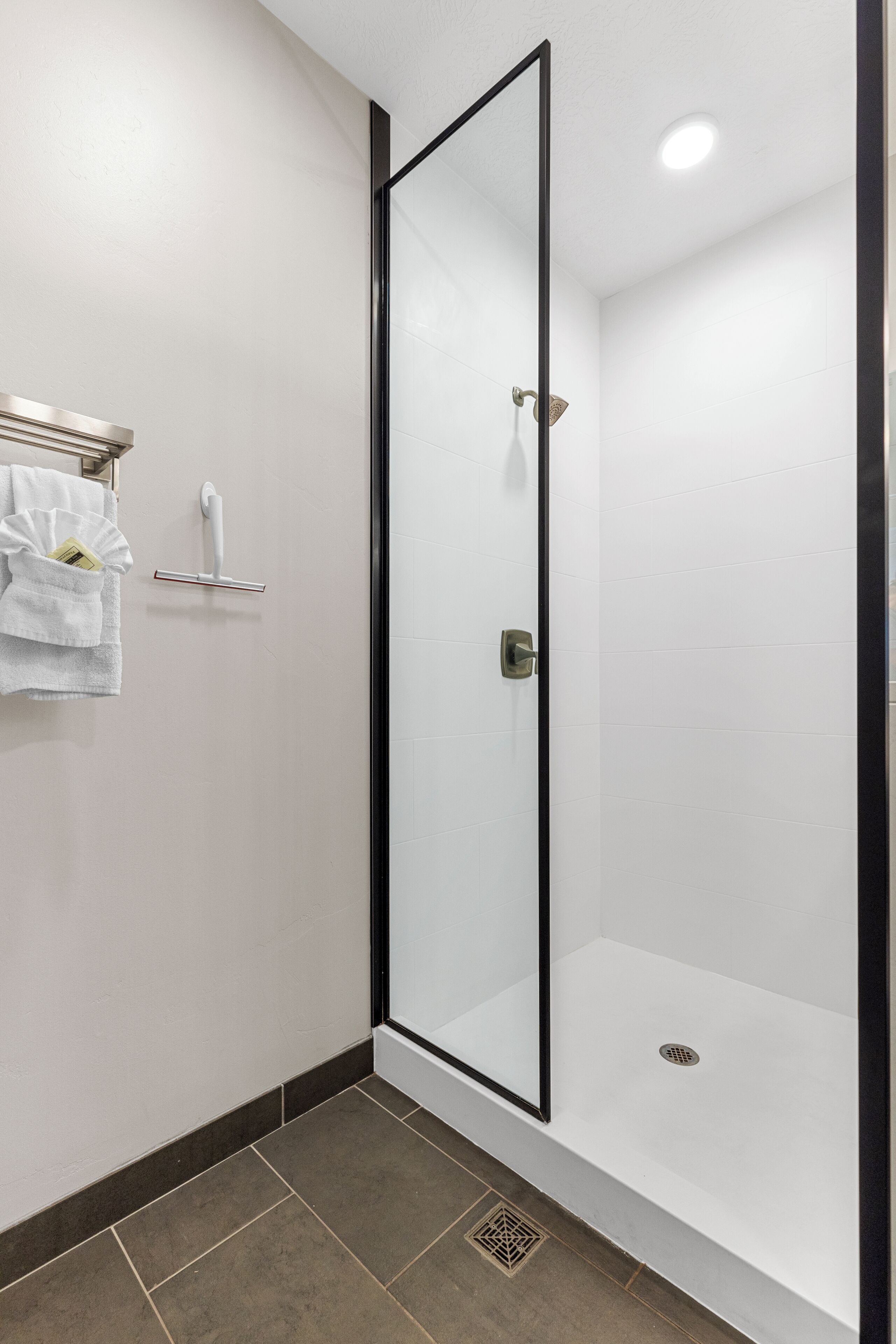 A modern bathroom with a glass-enclosed shower, a towel rack with a white towel, and a small shelf with a bottle.