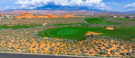A desert golf course with multiple green fairways and sand bunkers, surrounded by red rock formations and sparse vegetation.