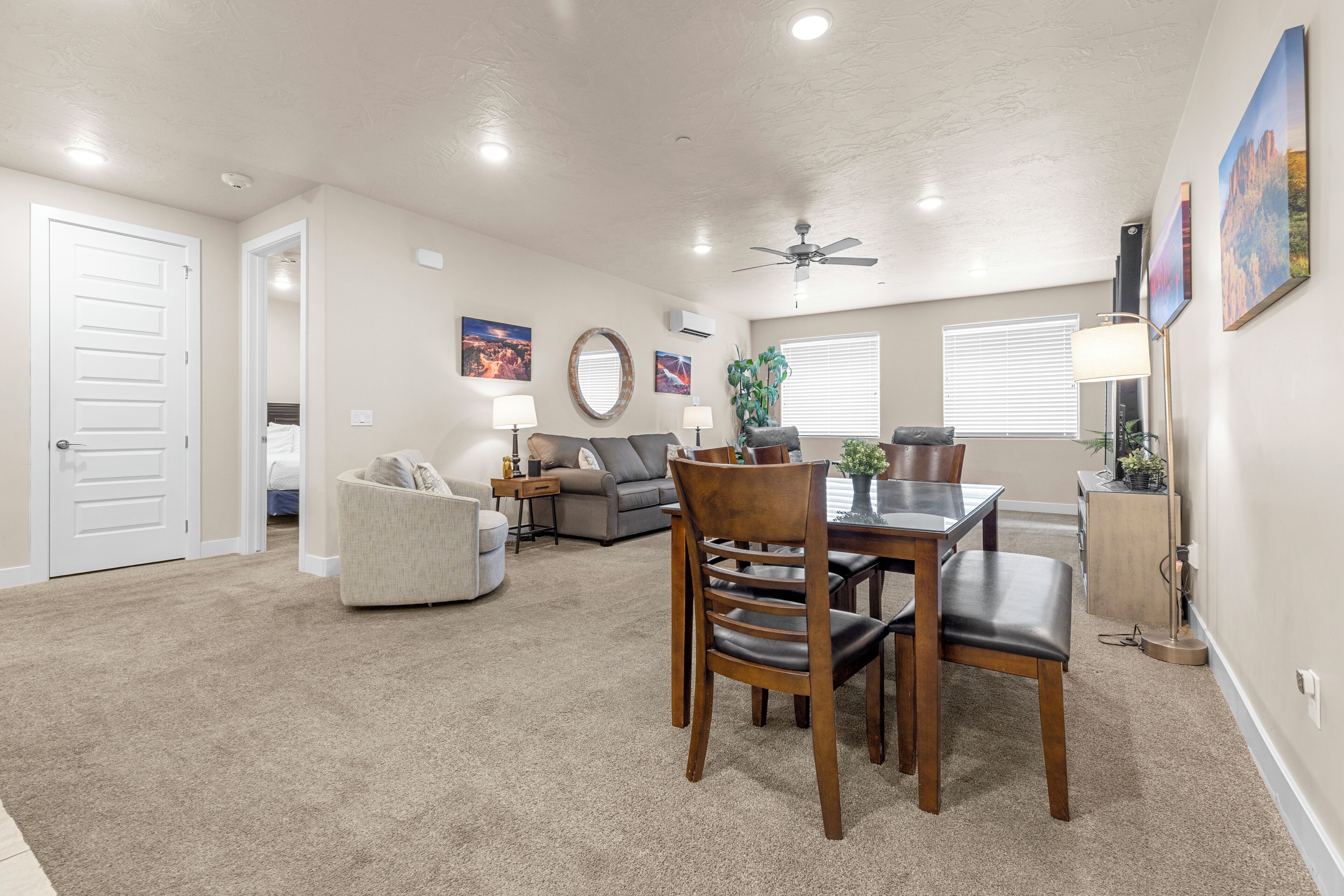 A spacious living room with a dining area, a ceiling fan, and a large window with blinds.