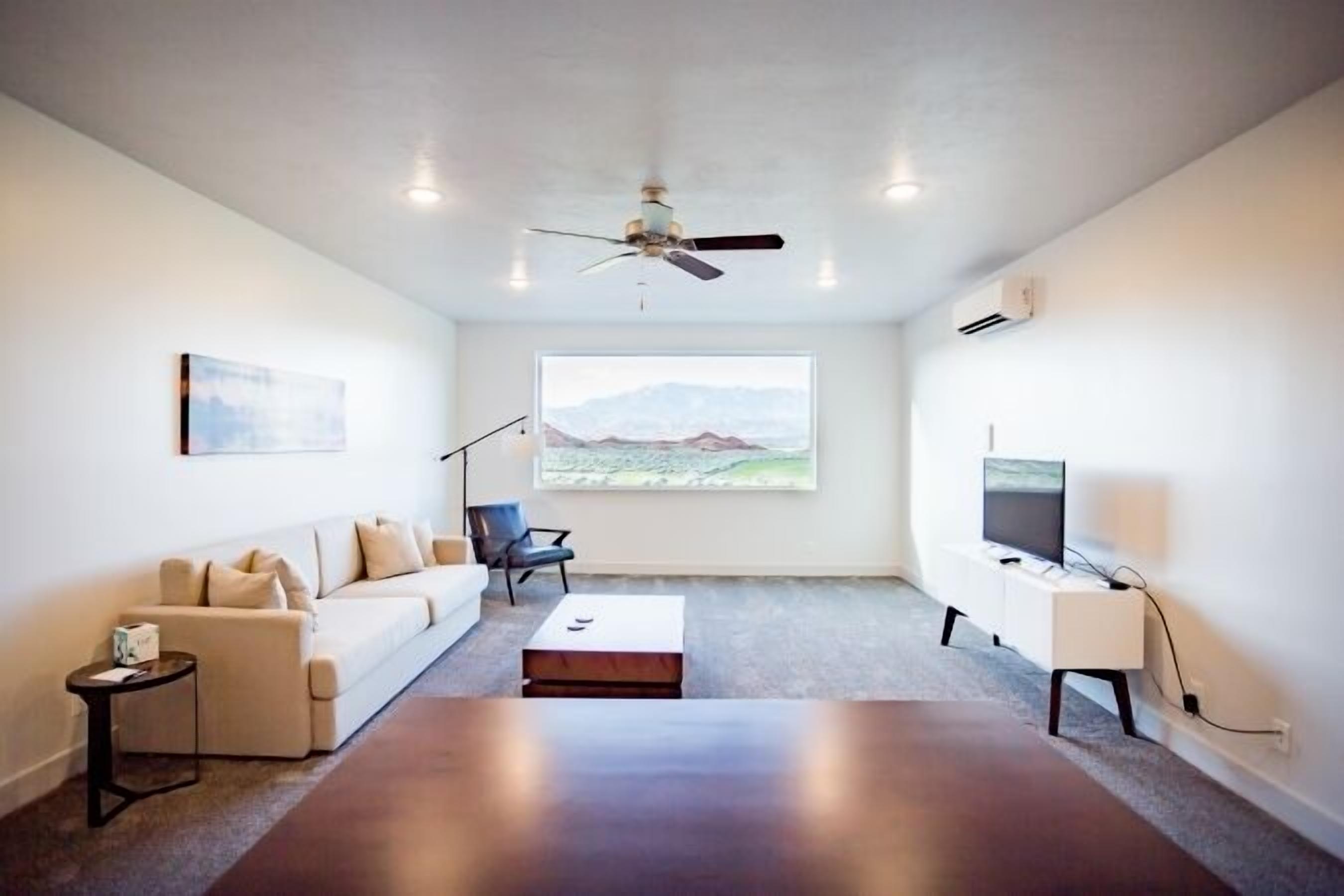 A modern living room with a sofa, a coffee table, a TV, and a large window with a mountain view.