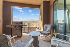 A balcony with a grill, chairs, and a table.