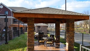 An outdoor patio area with a stone and wood pergola, a barbecue grill, and outdoor furniture. - Staybridge Suites Bowling Green by IHG (Bowling Green)