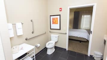 A bathroom with a toilet, handrails, a sink, and a shower area.