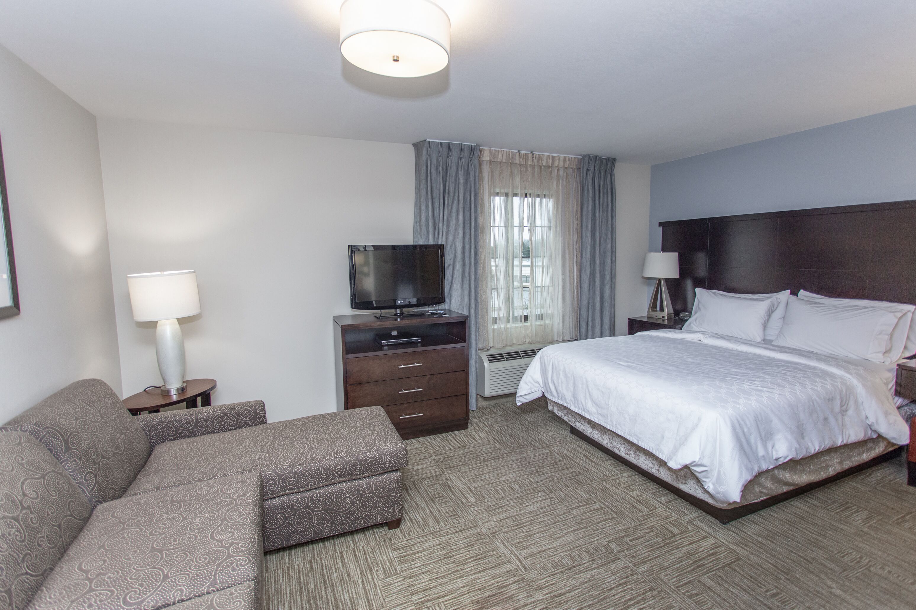 Quarto de hotel com cama, televisão, sofá, escrivaninha e luminária.