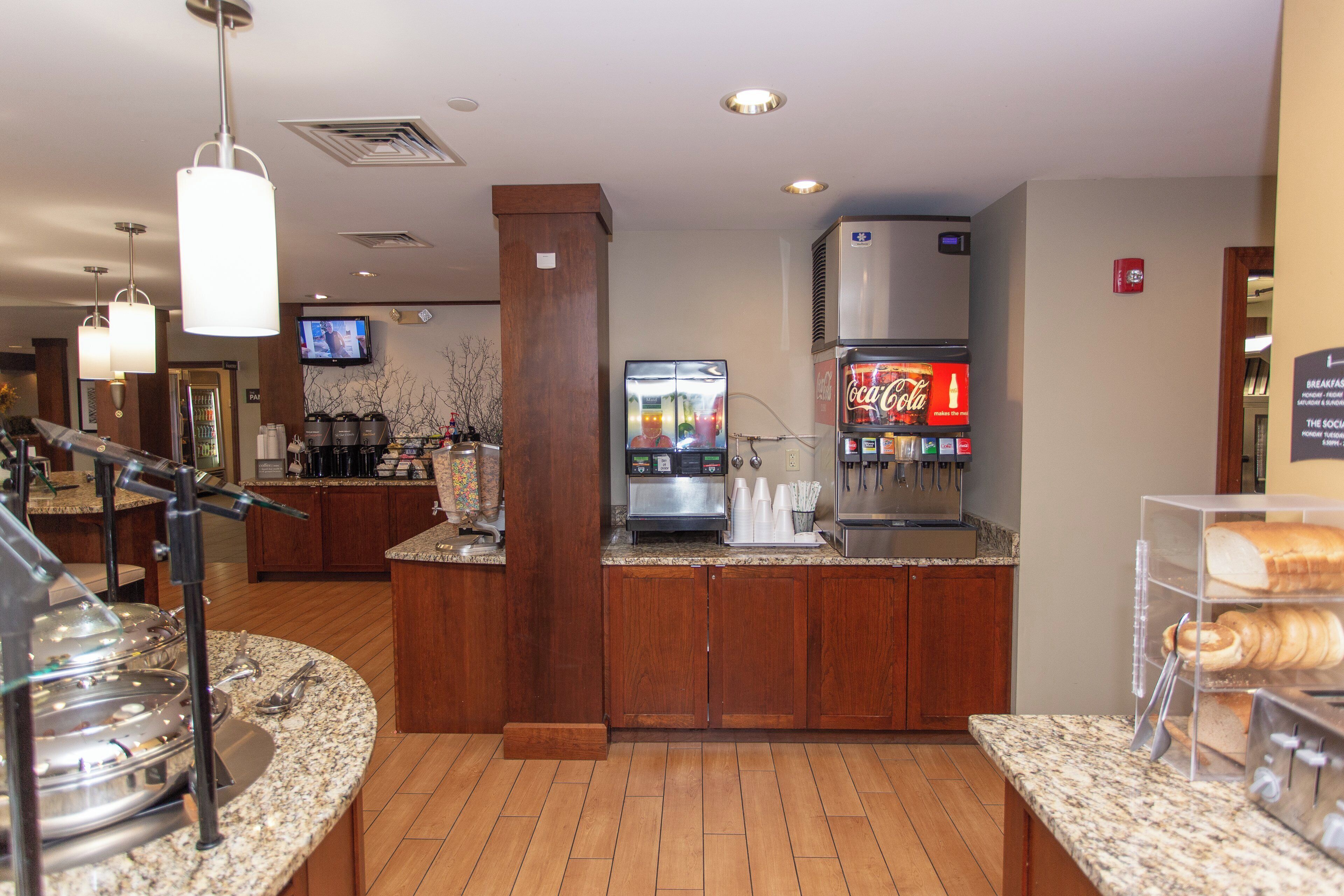 A hotel breakfast area with a coffee machine, refrigerator, and buffet setup.