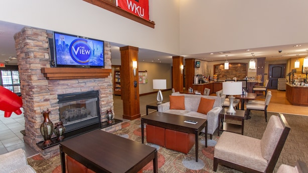 A spacious lobby with a stone fireplace, comfortable seating, a television mounted above it, and a banner with "WKU" on it. - Staybridge Suites Bowling Green by IHG (Bowling Green)