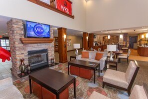 A spacious lobby with a stone fireplace, comfortable seating, a television mounted above it, and a banner with "WKU" on it. - Staybridge Suites Bowling Green by IHG (Bowling Green)