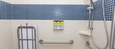 A bathroom with a shower, grab bars, and a soap dispenser.
